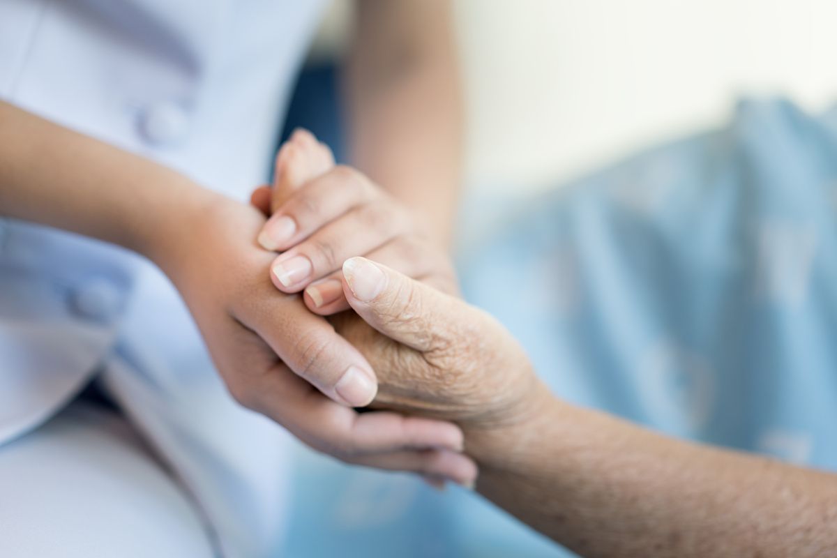 Nurse sitting on a hospital bed next to an older woman helping hands, care for the elderly concept2