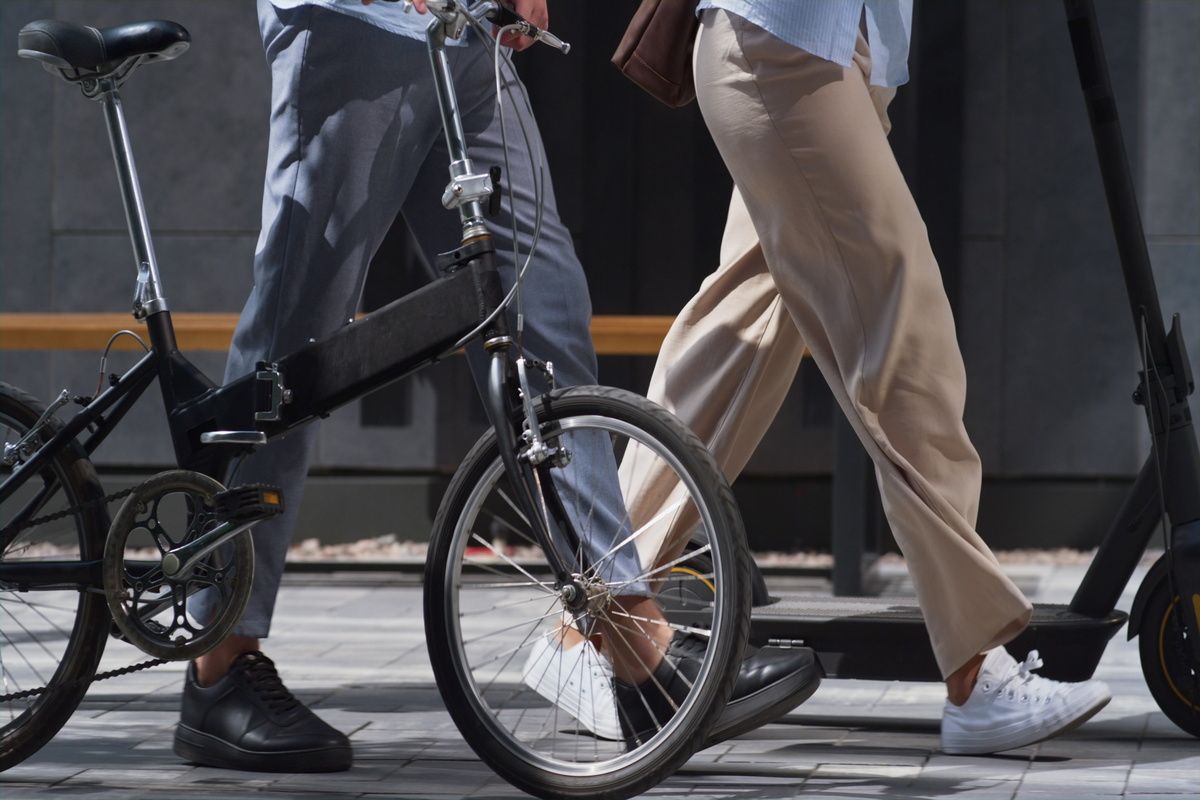 Workers legs walking downtown with electric scooter bicycle in hands close up.