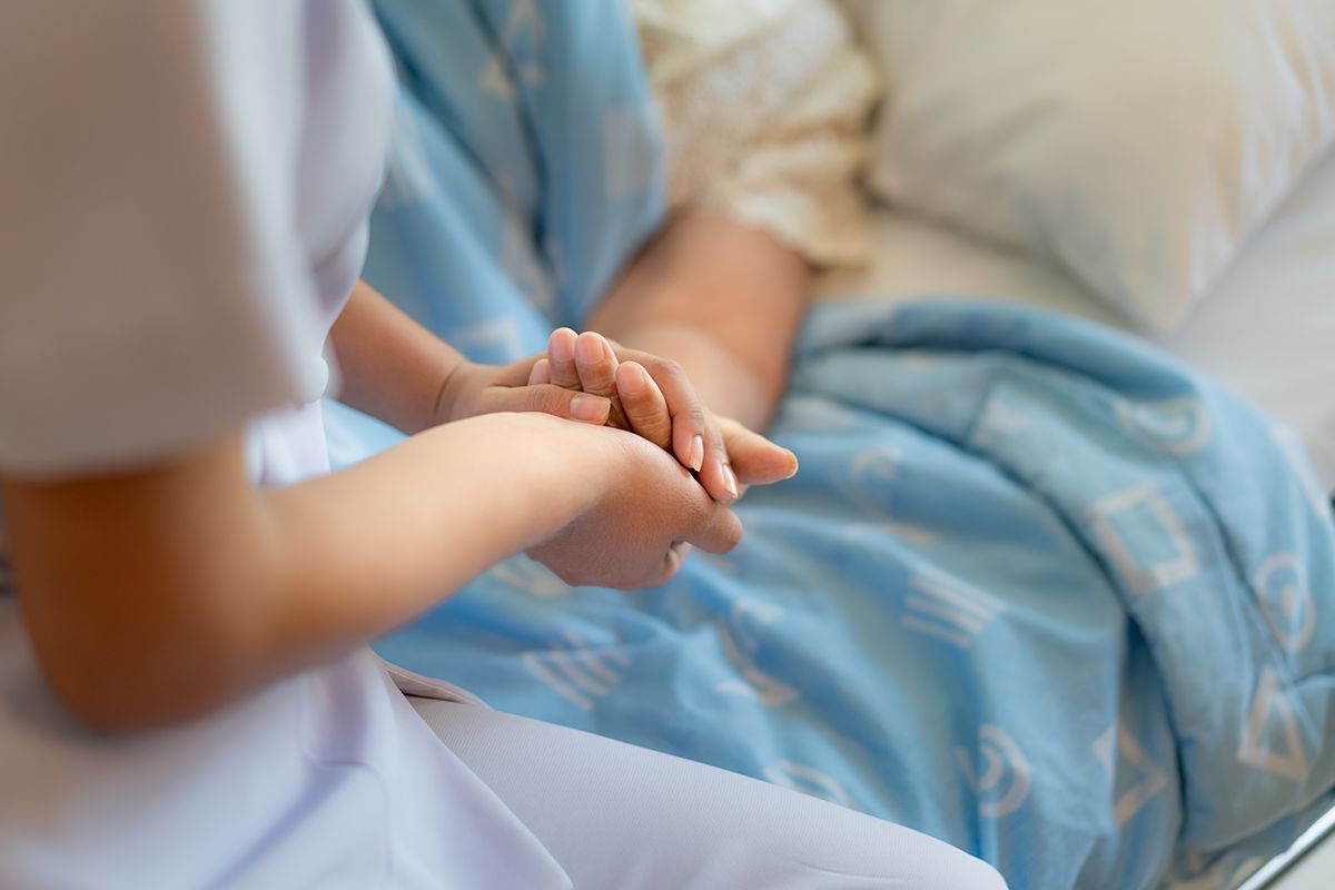 Pflegerin hält schützend die Hand einer zu pflegenden Person